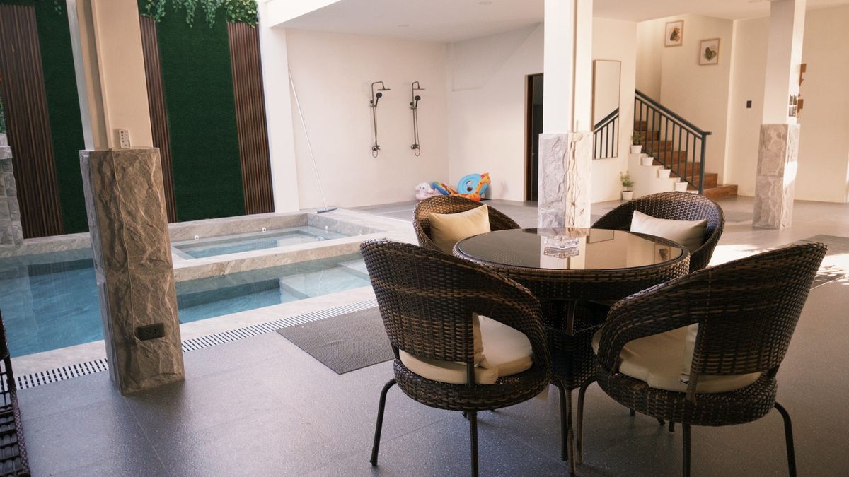 A wicker table and four chairs at the pool edge, the jacuzzi and steps behind them